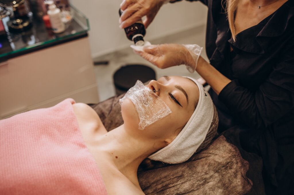 Cosmetologist applying mask on client's face in spa salon.